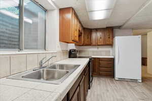 Basement secondary kitchen with stainless steel range with electric cooktop, tile counters, freestanding freezer, a sink, and light wood-type flooring