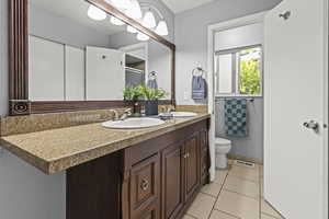 Full bathroom with double vanity, toilet, tile floors, and a shower