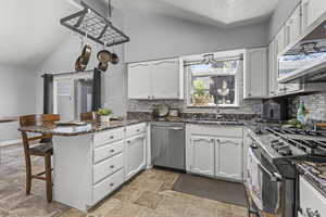 Kitchen featuring black range with gas stovetop, stainless steel microwave, a peninsula, a sink, and white cabinetry