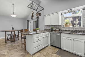 Kitchen featuring black range with gas stovetop, stainless steel microwave, a peninsula, a sink, and white cabinetry