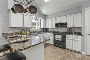 Kitchen featuring black range with gas stovetop, stainless steel microwave, a peninsula, a sink, and white cabinetry