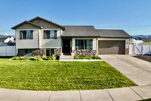 Tri-level home with an attached garage, a gate, concrete driveway, stone siding, and board and batten siding