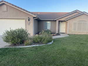 Ranch-style house with a garage, a tiled roof, stucco siding, and a front yard