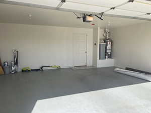 Garage featuring a garage door opener, gas water heater, and baseboards