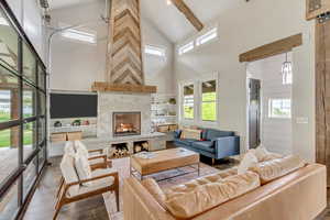 Living area featuring high vaulted ceiling, wood finished floors, a tiled fireplace, and beam ceiling