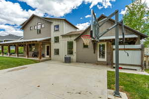 Rear view of house featuring board and batten siding, central AC unit, a patio, and a lawn