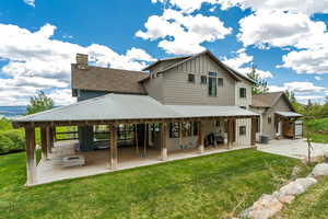 Rear view of property with board and batten siding, a patio, a lawn, and a chimney