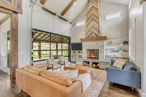 Living area with high vaulted ceiling, wood-type flooring, a tile fireplace, plenty of natural light, and beamed ceiling