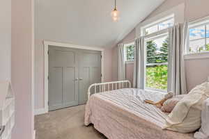 Bedroom with light colored carpet, vaulted ceiling, and a closet