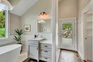 Master Bathroom with vanity, high vaulted ceiling, a soaking tub, and wood-type flooring