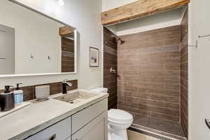 Bathroom with toilet, a tile shower, and vanity