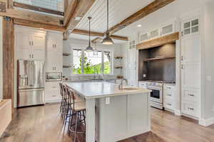 Kitchen with premium appliances, open shelves, a sink, wood-type flooring, and beamed ceiling