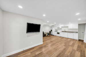 Unfurnished living room with a sink, baseboards, light wood-style flooring, and recessed lighting
