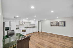 Kitchen with white appliances, white cabinetry, baseboards, recessed lighting, and light wood-style flooring