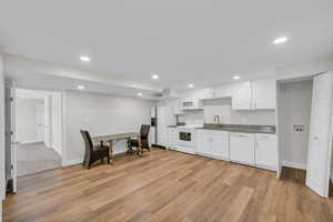 Kitchen featuring white appliances, a sink, white cabinets, light wood-style flooring, and recessed lighting