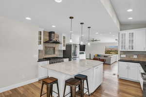 Kitchen featuring wall chimney exhaust hood, stainless steel fridge, backsplash, a center island, and white cabinets