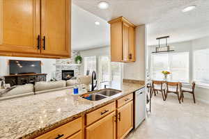 Kitchen featuring light stone countertops, a textured ceiling, open floor plan, dishwasher, and a fireplace