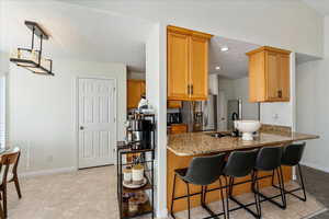 Kitchen featuring dark stone counters, stainless steel refrigerator with ice dispenser, decorative light fixtures, a breakfast bar area, and brown cabinets