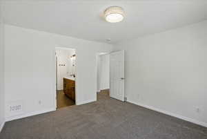 Unfurnished bedroom with dark colored carpet, baseboards, and connected bathroom