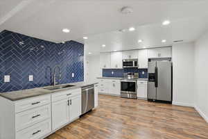 Kitchen featuring appliances with stainless steel finishes, a sink, backsplash, white cabinets, and wood finished floors