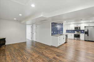 Kitchen featuring white cabinets, stainless steel appliances, a wood stove, tasteful backsplash, and dark wood finished floors