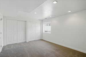 Unfurnished bedroom with carpet flooring, baseboards, recessed lighting, a textured ceiling, and multiple closets