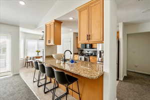 Kitchen with a textured ceiling, dark stone countertops, light carpet, stainless steel appliances, and a kitchen breakfast bar