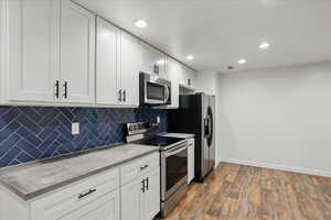 Kitchen featuring appliances with stainless steel finishes, white cabinetry, decorative backsplash, dark wood finished floors, and recessed lighting