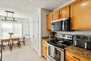 Kitchen featuring appliances with stainless steel finishes, a textured ceiling, hanging light fixtures, dark stone countertops, and light tile patterned flooring
