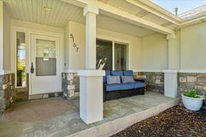 Entrance to property featuring stone siding, covered porch, and stucco siding