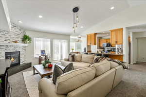 Carpeted living area featuring vaulted ceiling, a stone fireplace, recessed lighting, and a textured ceiling