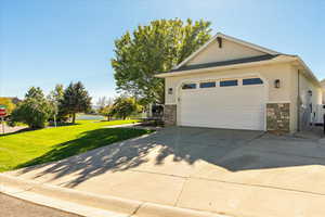 View of side of property with a yard, stone siding, stucco siding, and a garage