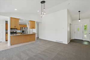 Kitchen featuring appliances with stainless steel finishes, light stone counters, open floor plan, light colored carpet, and high vaulted ceiling