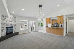 Unfurnished living room featuring vaulted ceiling, light carpet, a tiled fireplace, baseboards, and recessed lighting
