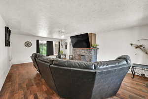 Living room with a textured ceiling, wood finished floors, and a stone fireplace