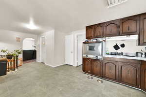 Kitchen featuring oven, under cabinet range hood, arched walkways, white stovetop, and dark brown cabinetry