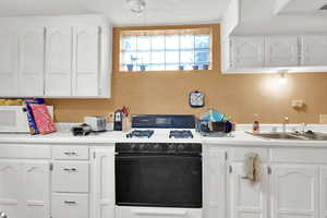 Kitchen featuring gas range, a sink, white cabinetry, and light countertops