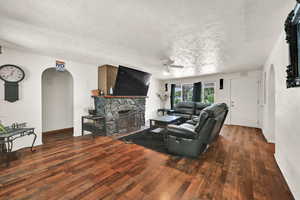 Living room featuring arched walkways, ceiling fan, a textured ceiling, wood-type flooring, and a fireplace
