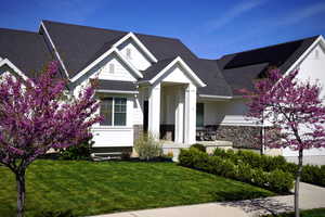View of front of home featuring stone siding, a front yard, and roof with shingles