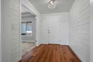 Foyer featuring a chandelier, wood walls, dark wood-style floors, and baseboards