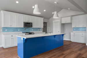 Kitchen with stainless steel microwave, a sink, stove, white cabinets, and vaulted ceiling