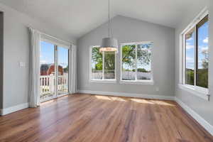 Unfurnished dining area with healthy amount of natural light, vaulted ceiling, wood finished floors, a chandelier, and baseboards