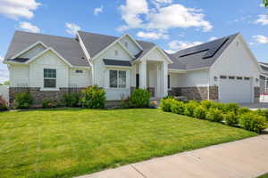 View of front of home featuring board and batten siding, stone siding, solar panels, a shingled roof, and a garage