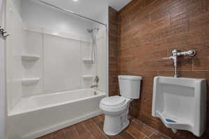 Full bathroom with bathtub / shower combination, toilet, wood-look tile walls, and wood finish floors