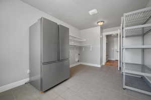 Laundry room featuring open shelves, baseboards, and light tile  flooring