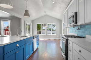 Kitchen with stainless steel appliances, a sink, blue cabinets, lofted ceiling, and light countertops