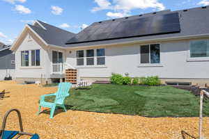 Back of property with a shingled roof, solar panels, stucco siding, and a yard