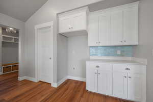 Kitchen with light countertops, vaulted ceiling, wood finished floors, decorative backsplash, and baseboards