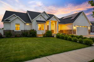 Modern inspired farmhouse with board and batten siding, stone siding, roof mounted solar panels, a front yard, and a garage