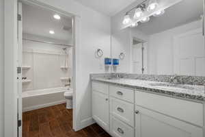 Bathroom with double vanity, wood finished floors, toilet, shower / tub combination, and baseboards